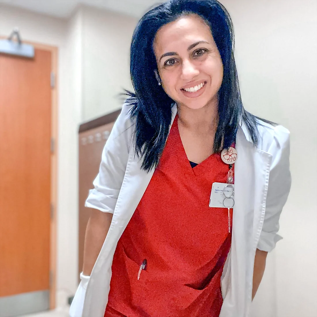 Tina, medical Speech-Language Pathologist, smiling in a clinical setting in red scrubs and a white coat
