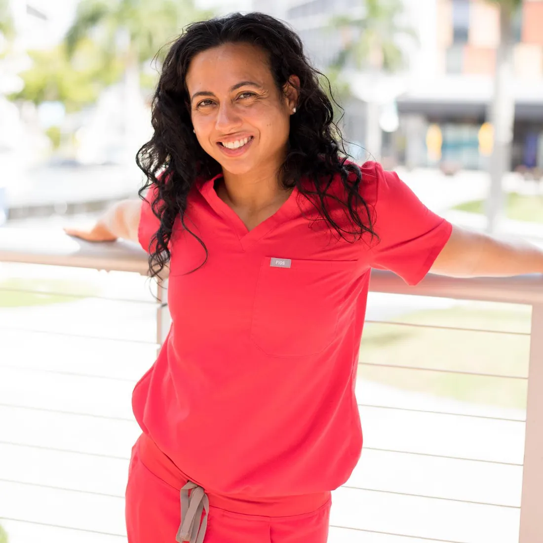 Tina in red scrubs smiling outdoors near a railing